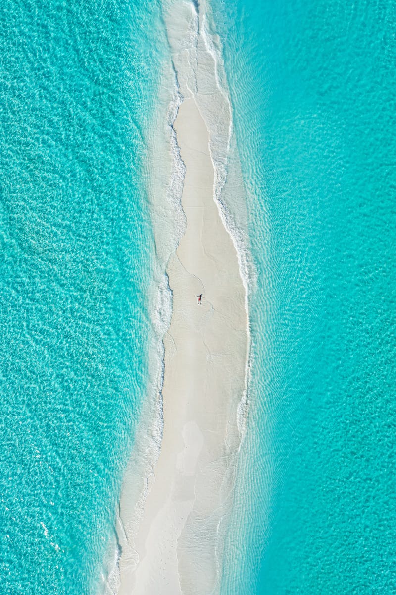 Drone shot of a serene sandy beach surrounded by vibrant turquoise ocean waves.