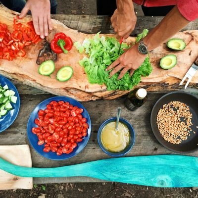 Fresh ingredients being prepared on a rustic wooden table, showcasing vibrant vegetables and hands at work.